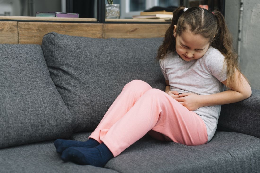 Criança sentida no sofá com dor abdominal, situação comum que leva famílias a buscar avaliação gastropediátrica
